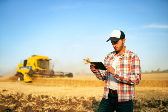 Precision farming. Farmer holding tablet for combine harvester guidance and control with modern automation system. Agronomist using online data management software generating yield maps at wheat field