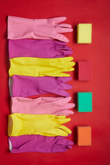 High angle view of rubber gloves and sponges lying in a row isolated on red background
