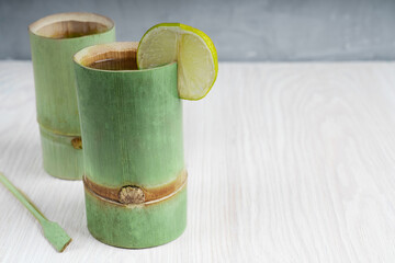Green natural bamboo glasses with water and lime slice are standing on light wooden table at kitchen