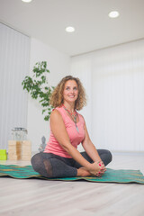 one young smiling middle aged woman practising yoga, indoors in yoga studio, in Sukhasana pose.