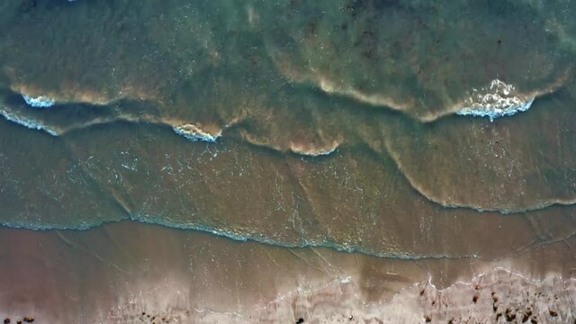 Rising top bird's eye aerial drone shot of small waves rolling onto golden sand from Well beach near Joao Pessoa in Northern Brazil.