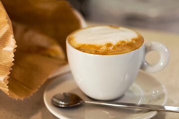 Close up of a cup of freshly prepared coffee with a steamed milk foam in a white cup with a spoon
