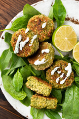 Vegan falafel with spinach and vegan yogurt dressing on a plate, top view