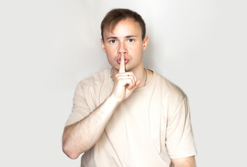 Portrait of a man close-up. Shows a hand gesture quietly, do not make noise, gesture a finger to the lips. On a light background. The concept of body language, human emotions, reaction.