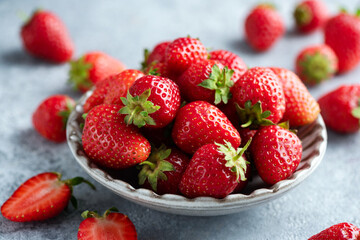 Fresh organic strawberries in bowl on concrete background. Organic fruits