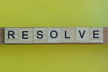 gray word resolve in small square wooden letters with black font on a yellow background