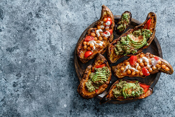 Baked sweet potato toast with roasted chickpeas, tomatoes, goat cheese, sauce guacamole, avocado, seedlings on wooden board over blue background. Healthy vegan food, clean eating, dieting, top view