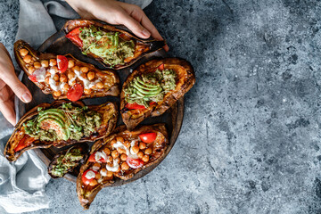 Hands holding the wooden board with baked sweet potato toasts with roasted chickpeas, tomatoes, avocado, seedlings. Healthy vegan food, clean eating, dieting, top view