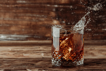 splashes in a whiskey glass on a wooden background.