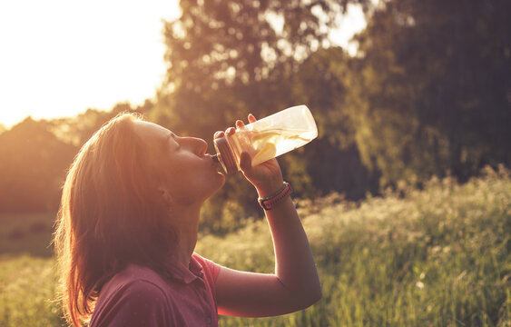 Girl drinking water with lemons from clear plastic bottle in contrast light during summer sunset