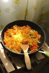 Preparation. Fried carrots and onions in a pan with a wooden spatula  on a wooden chair on a sunny day. Ray of light. Fried vegetables. Background image, copy space