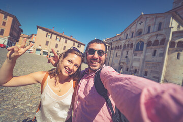 happy Tourist couple visit city center of Modena in the main square of the city taking selfie photo together. Major destination in Emilia-Romagna, Italy