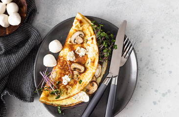 Homemade omelette with mushroom, mozzarella and microgreens on plate over light concrete background. Healthy food concept.
