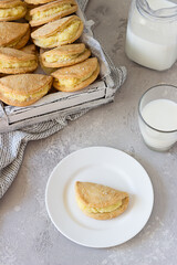 Homemade buns or pastries with cottage cheese on a wooden tray, light grey stone background. Traditional Russian pastry Sochnik. Selective focus.
