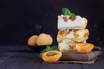 Delicious raw apricot cheesecake with crumble on wooden cutting board, dark background. Healthy...