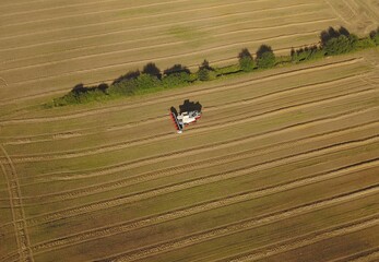 Obraz premium Fahrender Mähdrescher auf abgeernteten Getreidefelder mit einem Gehölzstreifen, Hecke dazwischen
