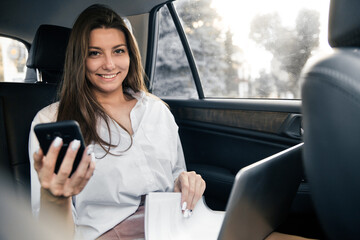 Smart business woman using phone and working on her laptop at the back sit of a car.