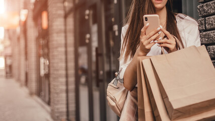 Beautiful fashionable woman using phone walking near mall with shopping bags.