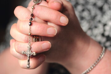 Lady's hands praying holding rosary beads with crucifix