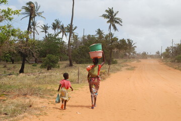 Kobieta z dzieckiem niosąca wodę szutrową drogą w Afryce w Mozambiku