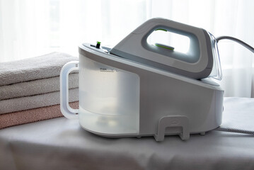 An electric iron with a steam generator and a stack of ironed towels on a light surface. Economics,...