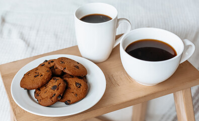 Breakfast in bed. Hot coffee with oatmeal cookies with chocolate on a wooden tray.