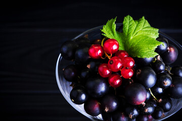 Black currant and green leaves on a dark wooden background. Background with currant berries and green leaves. Currant. Close-up