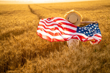 Back view of a girl in white dress wearing an American flag while running in a beautiful wheat field.