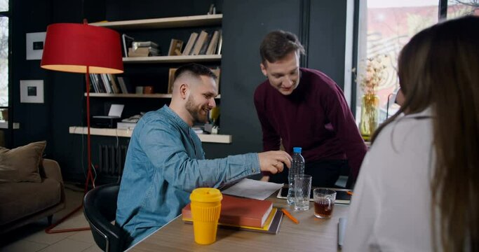 Successful young happy male Caucasian boss talking to male colleague celebrating achievement in modern healthy office.