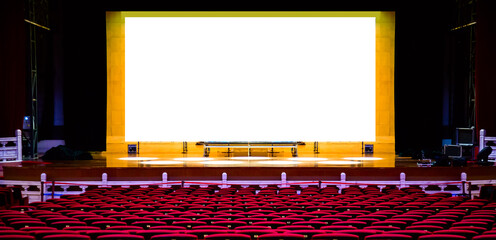 Concert or performance hall. Red seats armchairs and the stage before concert with blank white screen. Design mockup