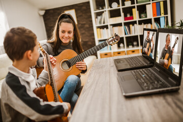 Boy and girl playing acoustic guitar and watching online course on laptop while practicing at home. Online training, online classes.