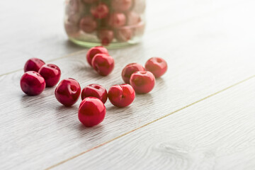 Fresh collected red cherry in a glass jar. Berries are scattered on a wooden background