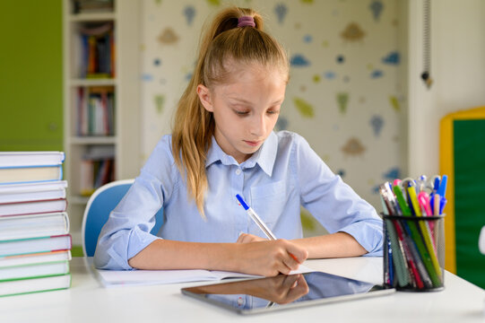 Girl does written lessons using the Internet. On the table next to the girl lies a tablet and textbooks.