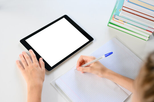 On the desk is a notebook, textbooks and a tablet with a blank display. The schoolgirl&rsquo;s right hand holds the pen, and the tablet&rsquo;s left hand controls the tablet.