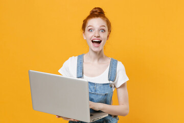 Naklejka premium Surprised young readhead girl in casual denim clothes white t-shirt isolated on yellow background studio portrait. People emotions lifestyle concept. Mock up copy space. Working on laptop pc computer.
