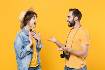 Shocked tourists couple friends guy girl in summer clothes, hat with photo camera isolated on yellow background. Passenger traveling abroad on weekends. Air flight journey concept. Speaking, talking.