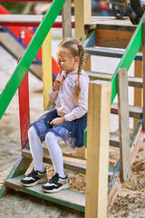 The girl sits on the steps of the house in the playground and smiles. girl in a light blouse and dark skirt
