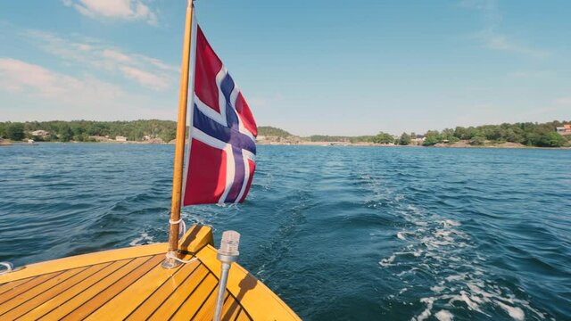 A Wooden Boat Sailing Across The Deep Blue Sea In Norway With A Norwegian Flag Astern - wide slowmo shot