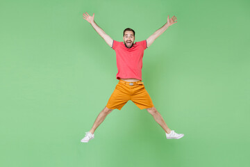 Fototapeta na wymiar full length Excited young bearded man guy in casual red pink t-shirt posing isolated on green background studio portrait. People lifestyle concept. Mock up copy space. Jumping spreading hands and legs
