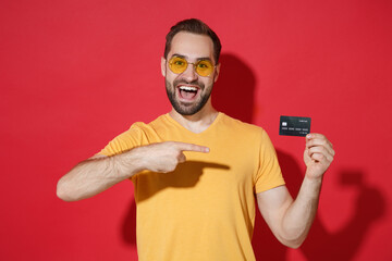 Funny young bearded man guy in casual yellow t-shirt glasses posing isolated on red wall background...