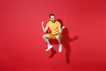 Fototapeta na wymiar Happy young bearded man guy in casual yellow t-shirt posing isolated on red background studio portrait. People sincere emotions lifestyle concept. Mock up copy space. Jumping doing winner gesture.