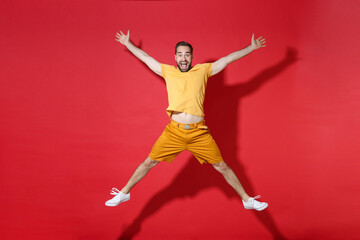 Excited young bearded man guy in casual yellow t-shirt posing isolated on red background studio portrait. People sincere emotions lifestyle concept. Mock up copy space. Jumping spreading hands legs.