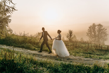 Beautiful wedding couple walk and hold hands during morning trip in mountains.