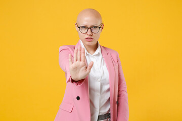 Serious young bald business woman in white shirt pink jacket glasses isolated on yellow wall...