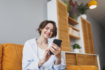 Smiling young woman girl in casual clothes sit on couch spending time in living room at home. Rest...