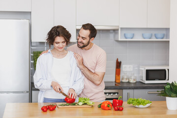 Obraz na płótnie Canvas Smiling young couple two friends guy girl in casual clothes preparing vegetable salad cooking food in light kitchen at home. Dieting family healthy lifestyle concept. Mock up copy space. Hugging.