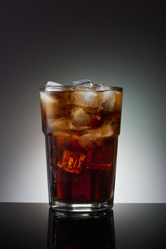 Tall glass with a cold dark drink, filled with pieces of ice,