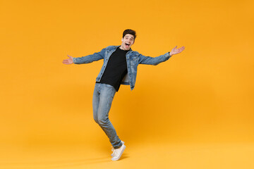 Fototapeta na wymiar full length Excited young man guy in casual denim clothes posing isolated on yellow wall background studio portrait. People emotions lifestyle concept. Mock up copy space Stand on toes spreading hands