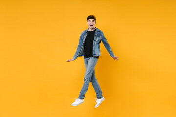 Fototapeta na wymiar full length Excited young man guy in casual denim clothes posing isolated on yellow background studio portrait. People sincere emotions lifestyle concept. Mock up copy space. Jump spreading hands legs