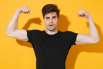 Strong young man guy 20s wearing casual black t-shirt posing isolated on yellow wall background...